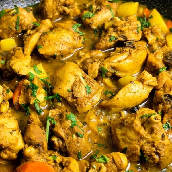 Close-up of chicken curry with potatoes, carrots, and herbs simmering in a black pan.